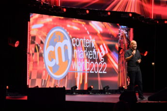 Light skinned black man wearing a black shirt and black pants on stage.  Content Marketing World 2022 on screen in the background.