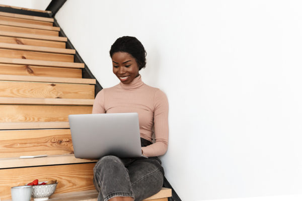 Black woman sitting on wooden stairs with a laptop in her lap.